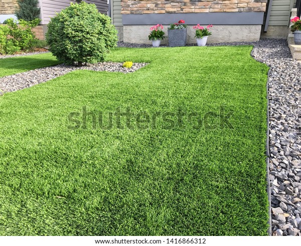 A beautiful artificial lawn in the\
front yard with nice flowers and shrubs surrounding\
it