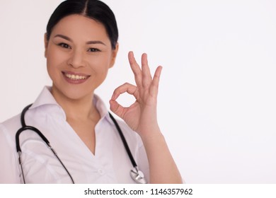 Beautiful Asain Medical Doctor Showing OK Sign. Happy Friendly Nurse Smiling Wide And Showing OK Sign To Camera Isolated On White Background.