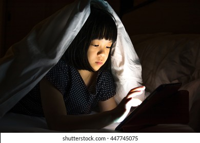 Beautiful Asia Small Female Kid Child Girl Sneaking Play Tablet Computer Pc Under Blanket At Night In A Dark Room. Adorable Elementary School Girl Sneak Playing Smartphone On Her Bed In Bedroom.