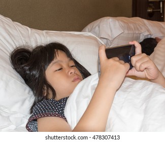 Beautiful Asia Small Female Kid Girl Sneaking Play Internet Mobile Phone On Bed At Night While Her Parent Sleeping.