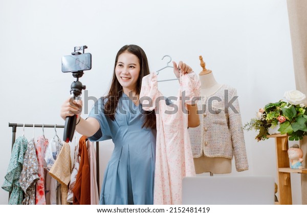 Beautiful Asia woman Live streaming selling\
clothes online with smartphone at her shop. Small business owner,\
online market\
concept.