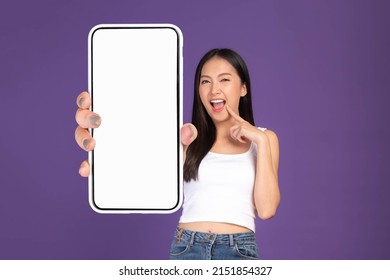 Beautiful Asian brunette woman cute girl in white tank top ,Excited surprised girl showing big smart phone with blank screen , white screen isolated purple background , Mock Up Image - Shutterstock ID 2151854327