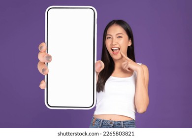 Beautiful Asian brunette woman cute girl in white tank top ,Excited surprised girl showing big smart phone with blank screen , white screen isolated purple background , Mock Up Image - Powered by Shutterstock