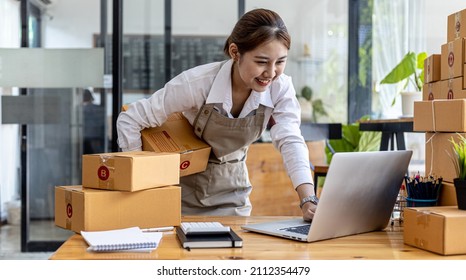 A Beautiful Asian Business Owner Opens An Online Store, She Is Checking Orders From Customers Via Laptop, Sending Goods Through A Courier Company, Concept Of A Woman Opening An Online Business.