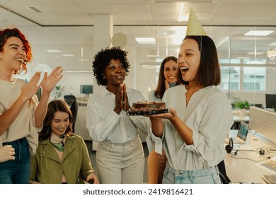 Beautiful asian business woman blowing out a candle on cake while celebrating birthday with multiracial coworkers in the office. Diverse colleagues gathered around the black birthday woman. Copy space - Powered by Shutterstock