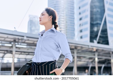 A beautiful Asian business woman is standing in a business district and looking ahead for something.