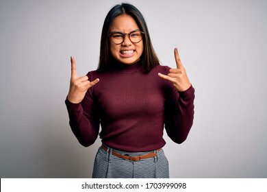 Beautiful Asian Business Woman Wearing Casual Sweater And Glasses Over White Background Shouting With Crazy Expression Doing Rock Symbol With Hands Up. Music Star. Heavy Concept.