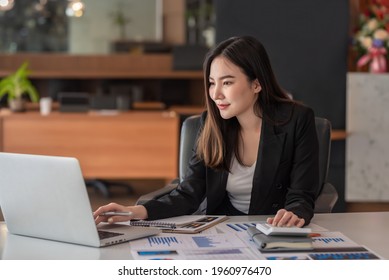 Beautiful Asian Businesswoman Analyzes Charts Using Laptop Calculator At The Office.