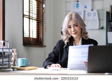 Beautiful Asian Businesswoman Analyzes Charts Using Laptop Calculator At The Office.
