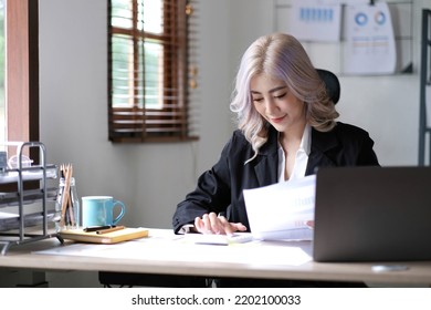 Beautiful Asian Businesswoman Analyzes Charts Using Laptop Calculator At The Office.
