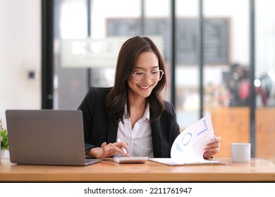 Beautiful Asian Businesswoman Analyzes Charts Using Laptop Calculator At The Office.