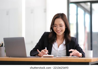 Beautiful Asian Businesswoman Analyzes Charts Using Laptop Calculator At The Office.