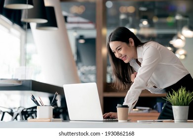 Schöne asiatische Geschäftsfrau feiert mit Laptop im Büro und zeigt Freude. Kleineres Startup-Unternehmen und erfolgreiches Konzept. 