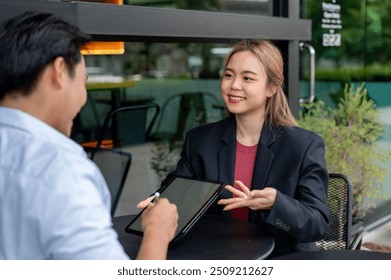 A beautiful Asian businesswoman or insurance agent is having an informal meeting with her client at a coffee shop, discussing and showing information on her digital tablet. - Powered by Shutterstock