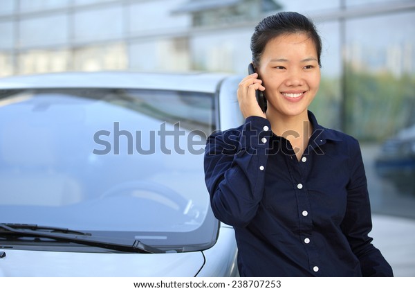 beautiful asian businesswoman on the phone\
leaning on car outside of office building\
