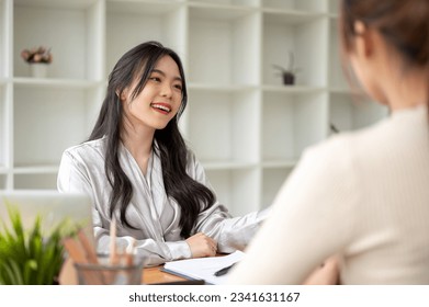 A beautiful Asian businesswoman is talking with her colleague at a table in the office. A professional female job recruiter or HR interviewing a candidate in the office. - Shutterstock ID 2341631167