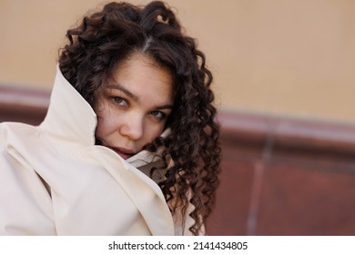 Beautiful Asian Caucasian Woman Covering Her Face With Beige Coat Outdoors In Street, Spring, Sun Shining. Woman Closed And Distrustful And Frightened	
