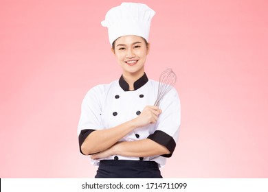 Hermosa cocinera asiática sonríe y sostiene el whisky de globo inoxidable aislado en un fondo rosa, Felicidad y Alegre chef profesional Concepto