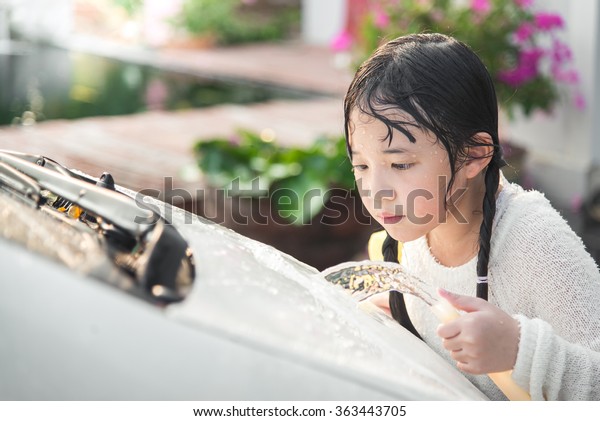 Beautiful asian\
child washing car in the\
garden