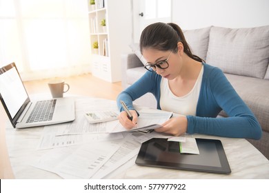 Beautiful Asian Chinese Woman Using Laptop And Digital Table Touch Pad To Calculate Bills Sitting On Sofa In The Living Room At Home. Interior And Domestic Housework Concept.