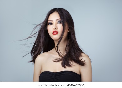 Beautiful asian coasian woman with long hair posing in studio on grey background. Women Hair Is Fluttering In The Wind.