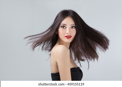 Beautiful Asian Coasian Woman With Long Hair Posing In Studio On Grey Background. Women Hair Is Fluttering In The Wind.