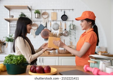 Beautiful Asian Delivery Woman In An Orange Uniform Send Package Products For Cook Customers In Kitchen. Domestic And International Transport And Logistics