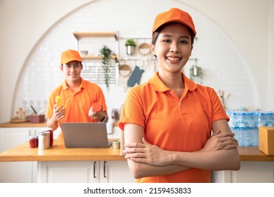 Beautiful Asian Delivery Woman In An Orange Uniform Embrace For Show Leadership To Build Confidence For Cook Customers In Kitchen. Domestic And International Transport And Logistics Service