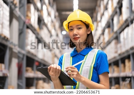 Beautiful asian engineer woman wearing safety helmet and reflective vest, She checking goods supplies on shelves with tablet in ware house and looking camera. Logistic and business export concept.	