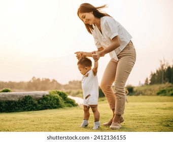 A beautiful Asian family enjoying a sunny day in the park as they teach their baby to take his first steps. Cute toddler little child family concept - Powered by Shutterstock