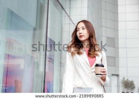 Beautiful asian female businesswoman hold paper cup of hot drink, Walk enjoy smiling while doing commuting in the modern city near office building outside