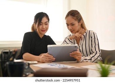 Beautiful asian female employee sharing ideas business strategy, discussing online information on digital tablet with colleague - Shutterstock ID 2254957951