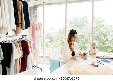 Beautiful Asian female fashion designers or dressmakers make phone calls with a customer for the new collection with samples of fabrics and sketches on paper. Fashion designer working in the studio. - Powered by Shutterstock