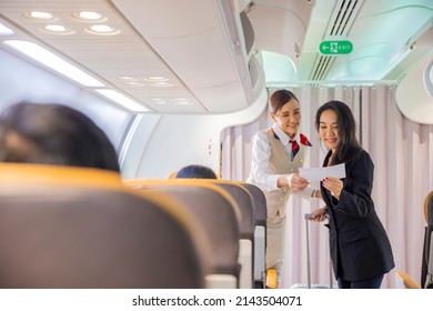 Beautiful Asian female flight attendants in uniform standing at the airplane entrance service take care of asian woman passengers checking seats boarding pass on the airplane before flight traveling. 