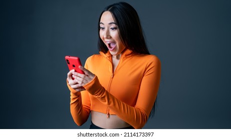 Beautiful Asian Female Isolated On A Grey Background Using A Mobile Phone. Portrait Of A Woman Looking Surprised To See A Message From Someone, Happy And Excited, Using Smartphone Device.