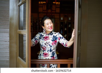 Beautiful Asian female opening window with a huge smile.China lady wearing qipao in traditional setting.Happy woman with red lipstick during festival. Chinese New Year celebration.