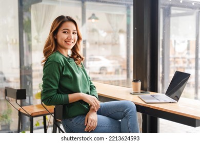 Beautiful Asian Girl Enjoys Coffee While Working In A Coffee Shop On Laptop Connected To Public Wifi. Stylish College Student Studying Online While Spending Free Time In The Park.