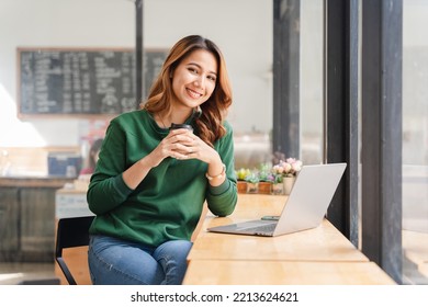 Beautiful Asian Girl Enjoys Coffee While Working In A Coffee Shop On Laptop Connected To Public Wifi. Stylish College Student Studying Online While Spending Free Time In The Park.