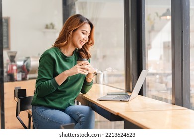 Beautiful Asian Girl Enjoys Coffee While Working In A Coffee Shop On Laptop Connected To Public Wifi. Stylish College Student Studying Online While Spending Free Time In The Park.