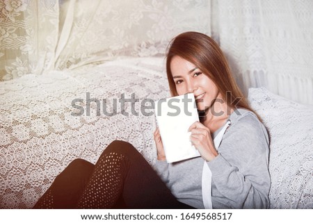 Beautiful Asian girl happy to reading book for education for knowledge and learning, She sit on sofa and smile. The book blank for the wording and message 