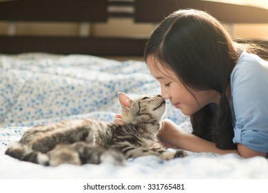 Beautiful asian girl kissing american shorthair cat on the bed