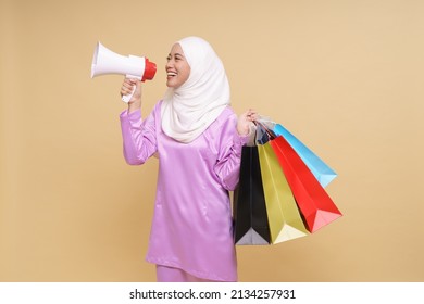 Beautiful Asian Girl In Purple Dress And Hijab Holds In Hand Bullhorn Public Address Loud Hailer With Shopping Bags On Beige Background. Scream In Megaphone. Business Shopping Sales Lifestyle Concept.