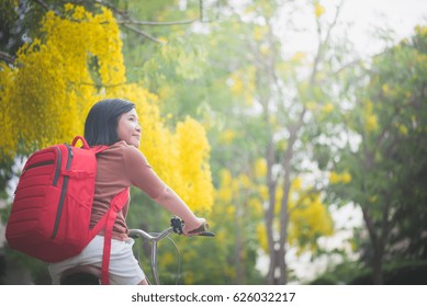 Beautiful Asian girl with red backpack riding bicycle in the park,Thailand travel concept Stock Photo