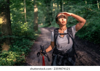 beautiful asian girl shields her eyes from the sun with her hand, hiking watching birds concept. Asian woman hiking in the woods, she is shielding her eyes to look for birds - Powered by Shutterstock