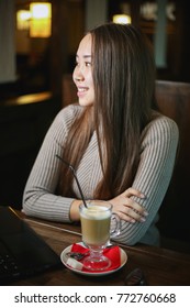 Beautiful Asian girl sitting at cafe with laptop and drinking aromatic coffee