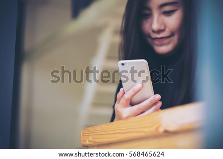Beautiful Asian girl with smiley face using smart phone in modern cafe