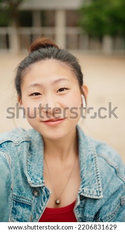 Beautiful Asian girl taking selfie outdoors. Pretty Japanese woman making content for her blog on the street. Modern technology