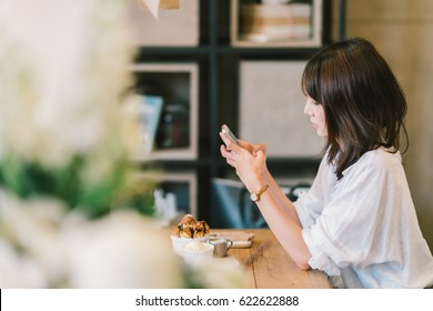 Beautiful Asian girl using smartphone at cafe with chocolate toast, ice cream, and milk syrup. Coffee shop dessert and modern casual lifestyle or mobile phone technology concept. With copy space