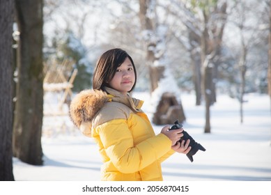 Beautiful Asian girl  in warm clothes with camera shooting a photo in the winter park
