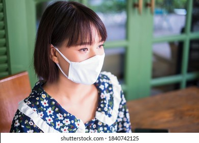 Beautiful Asian Girl Wearing Facemask Protection Contagious Coronavirus Covid-19, Using Smart Phone Mobile Online Internet Café Relaxing, Stay Safe Healthy Socializing In Public Area Social Distancing